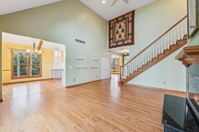 unfurnished living room with stairs, ceiling fan with notable chandelier, wood finished floors, high vaulted ceiling, and visible vents