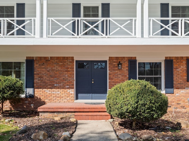 doorway to property with covered porch, brick siding, and a balcony
