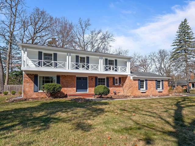 view of front facade with fence, a front yard, brick siding, and a balcony