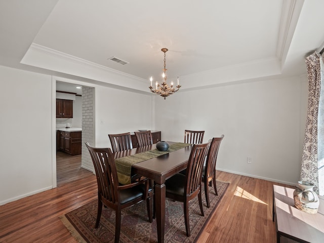 dining space with a tray ceiling, ornamental molding, visible vents, a chandelier, and wood finished floors