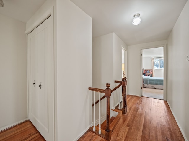hallway featuring wood finished floors, an upstairs landing, and baseboards