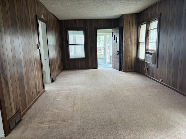 unfurnished room with light colored carpet, wooden walls, visible vents, and a textured ceiling