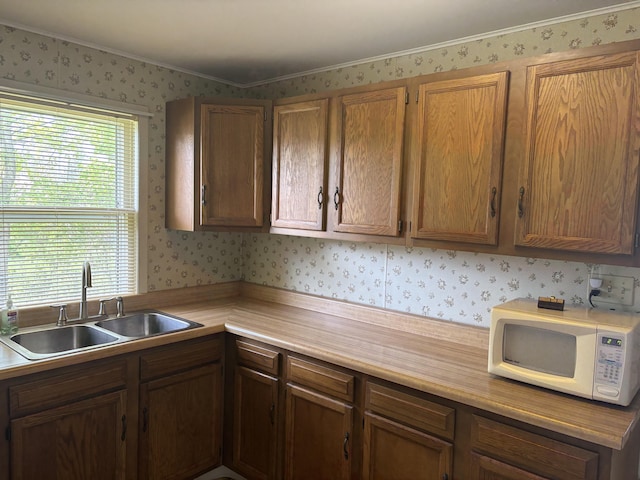 kitchen with light countertops, white microwave, wallpapered walls, and a sink
