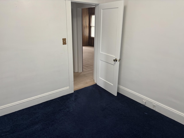 unfurnished room featuring baseboards and dark colored carpet