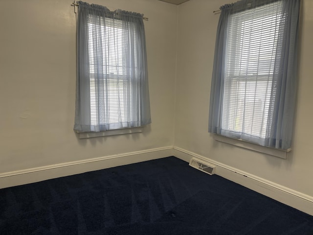 spare room featuring baseboards, dark colored carpet, and visible vents