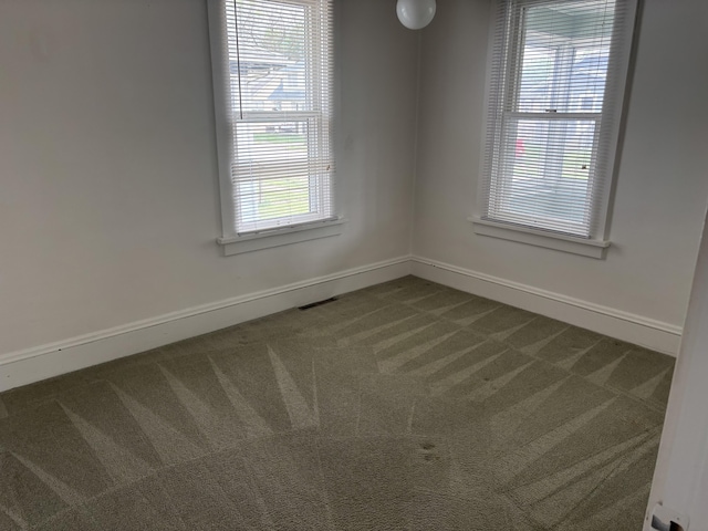 spare room featuring baseboards, dark carpet, and visible vents