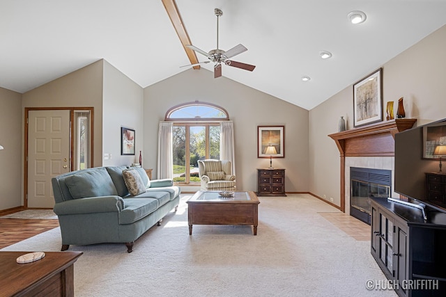 living area with a tile fireplace, a ceiling fan, high vaulted ceiling, baseboards, and light colored carpet