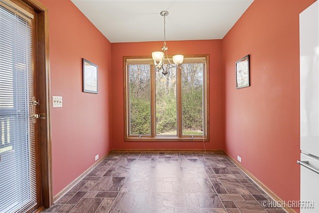 unfurnished dining area featuring baseboards, stone finish flooring, and an inviting chandelier