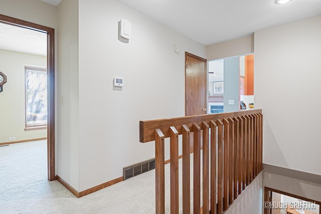 hallway featuring baseboards, light carpet, and an upstairs landing