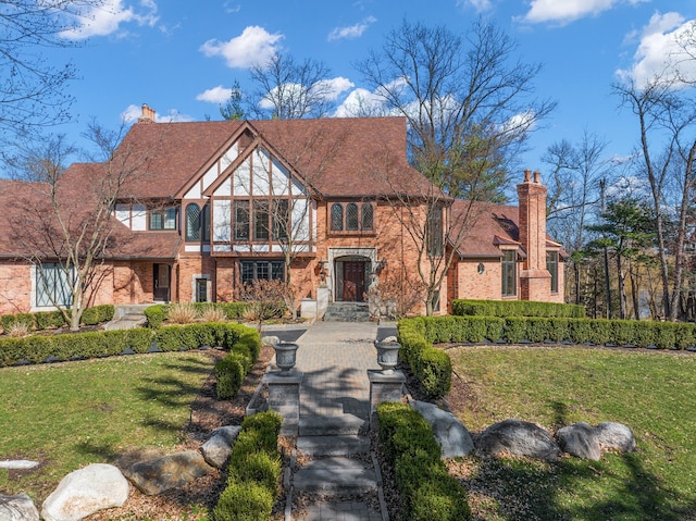 tudor home with a front lawn, brick siding, and a chimney