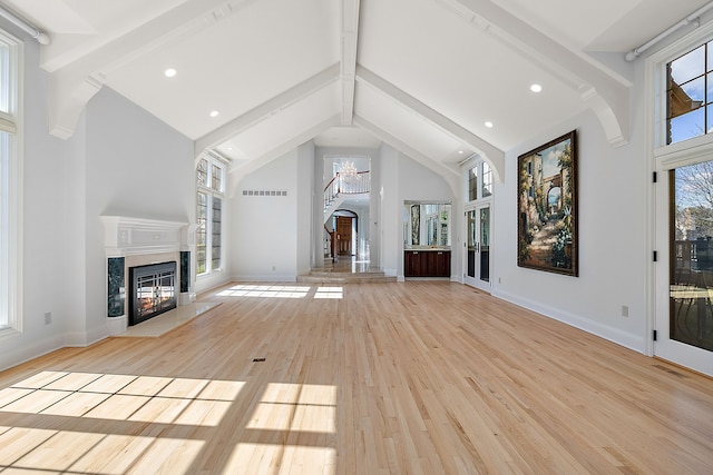 unfurnished living room with light wood-style flooring, high vaulted ceiling, a fireplace, baseboards, and beamed ceiling