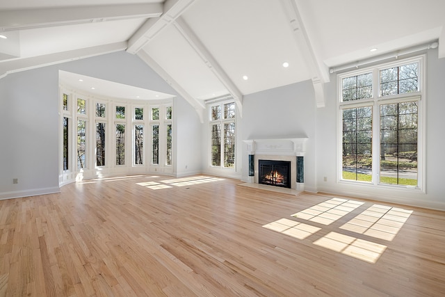 unfurnished living room with high vaulted ceiling, beamed ceiling, a lit fireplace, baseboards, and light wood-style floors