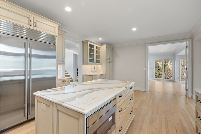 kitchen featuring built in appliances, light stone counters, cream cabinetry, crown molding, and light wood-style floors
