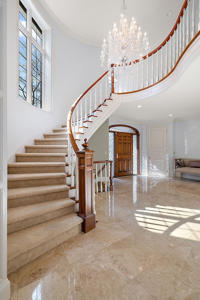 foyer with stairs, a chandelier, crown molding, and a high ceiling