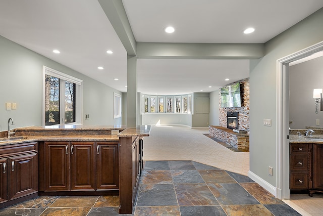 kitchen with a sink, stone tile floors, a fireplace, and dark brown cabinets