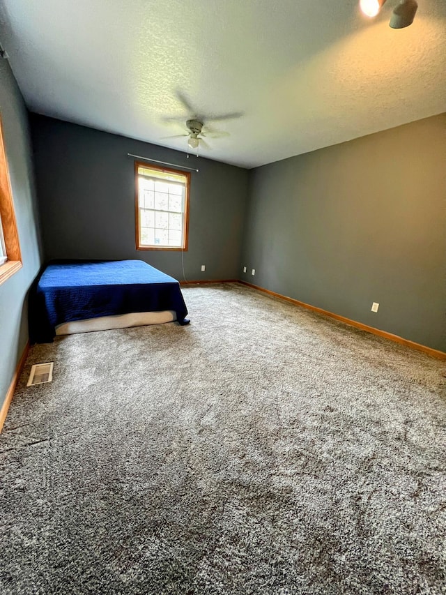 unfurnished bedroom with carpet, a textured ceiling, visible vents, baseboards, and ceiling fan
