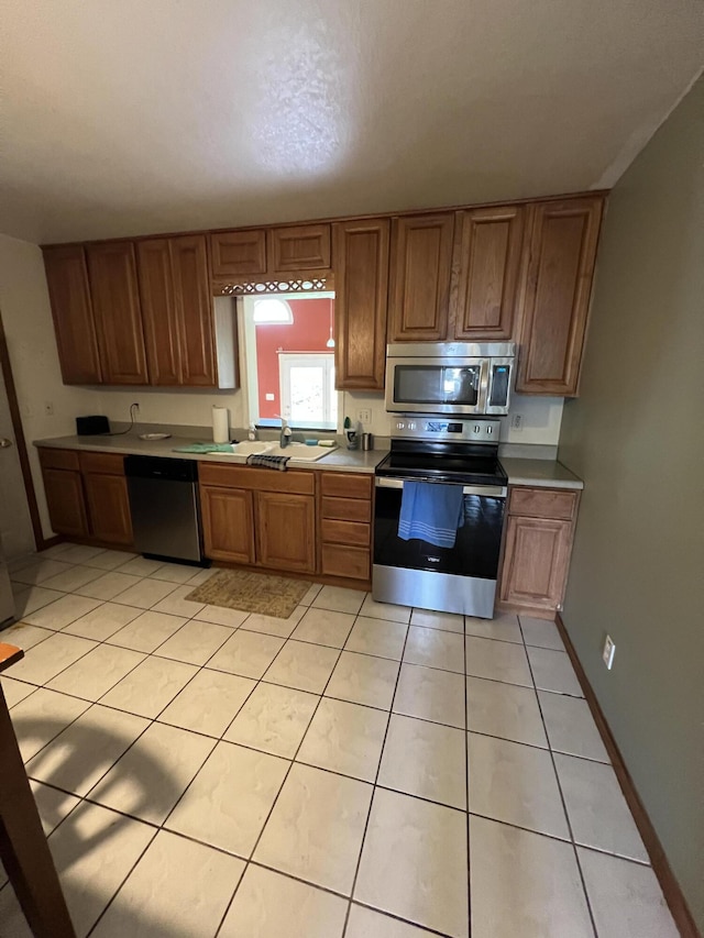kitchen with brown cabinetry, light tile patterned flooring, light countertops, and appliances with stainless steel finishes