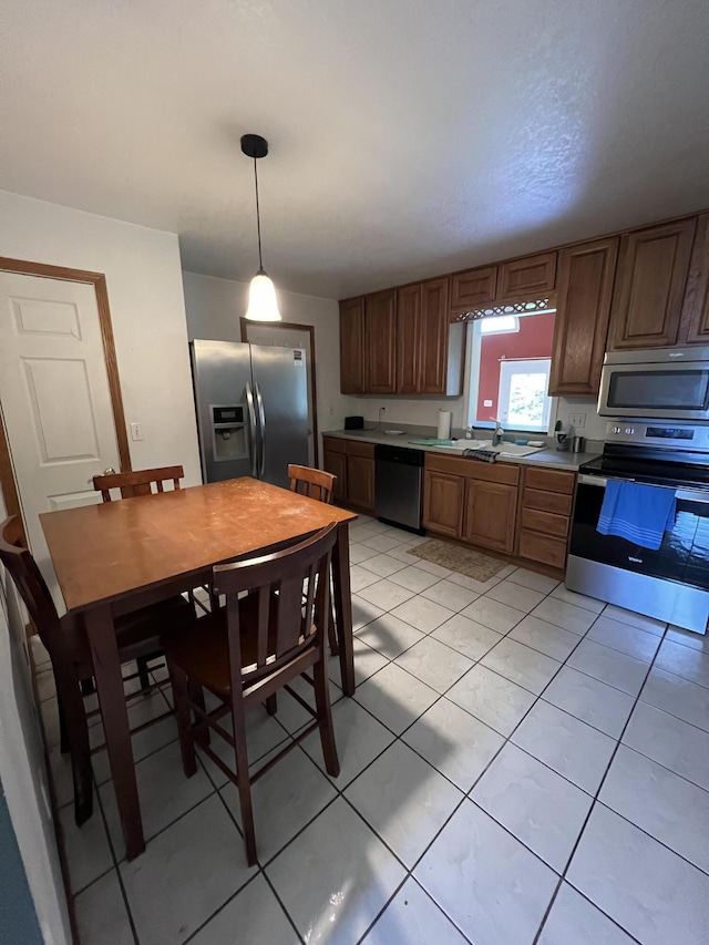 kitchen featuring light tile patterned floors, a sink, stainless steel appliances, decorative light fixtures, and light countertops