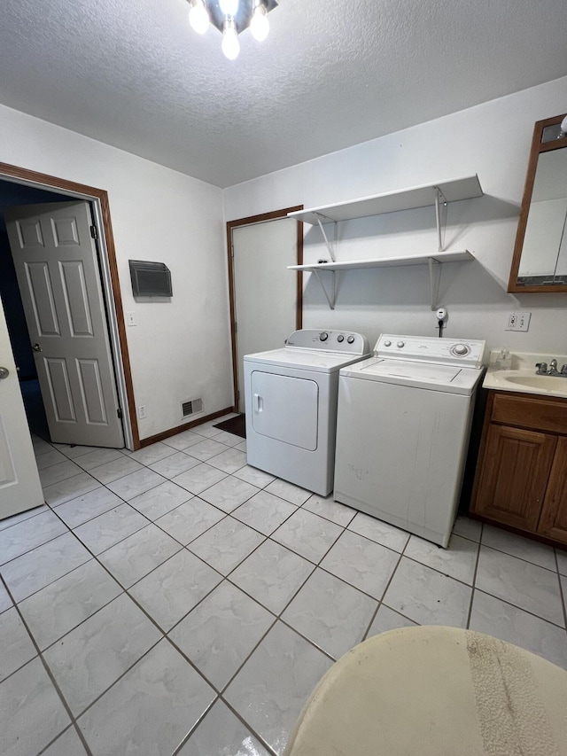laundry room featuring a sink, cabinet space, a textured ceiling, washer and clothes dryer, and visible vents