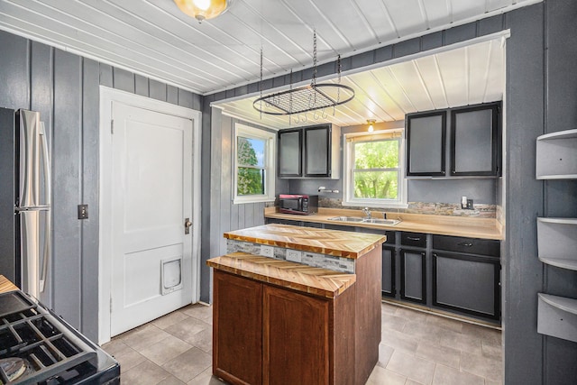 kitchen featuring wood counters, freestanding refrigerator, a sink, light tile patterned floors, and a center island