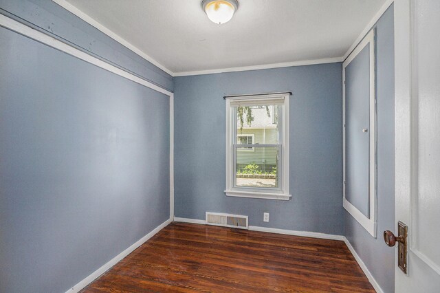 empty room with wood finished floors, crown molding, and baseboards