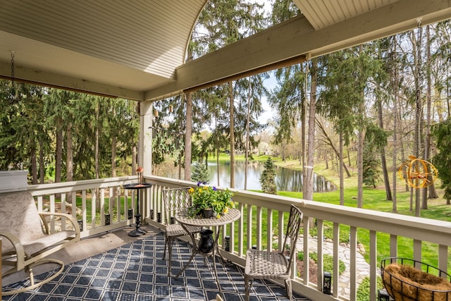 wooden terrace with a water view, view of wooded area, and a lawn