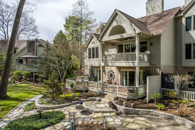 rear view of property featuring a balcony, brick siding, a chimney, a shingled roof, and a wooden deck