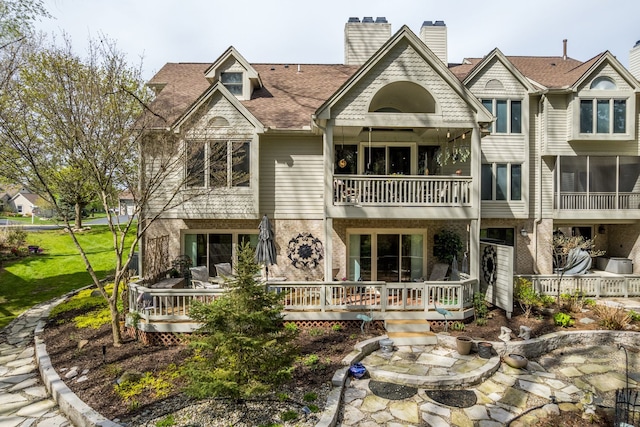 back of property featuring a balcony, roof with shingles, brick siding, and a chimney