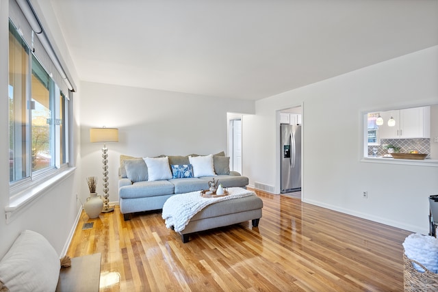 living room with light wood-style floors, visible vents, and baseboards