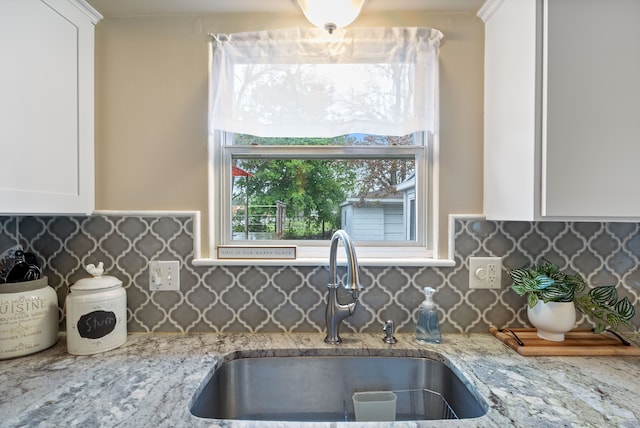 kitchen with a sink, light stone countertops, white cabinetry, and tasteful backsplash