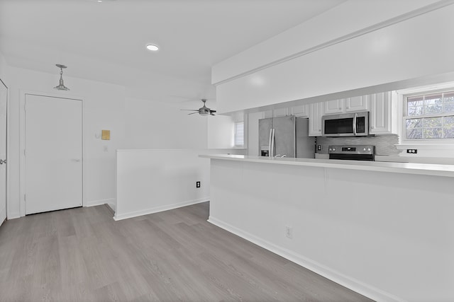 kitchen featuring light wood finished floors, a ceiling fan, decorative light fixtures, light countertops, and appliances with stainless steel finishes