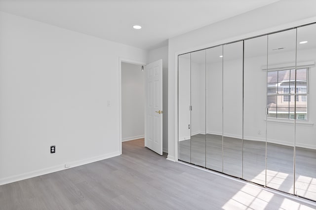 unfurnished bedroom with a closet, wood finished floors, baseboards, and recessed lighting