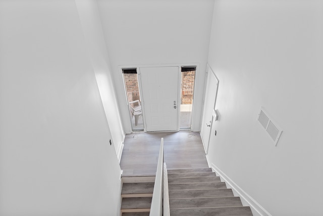 stairs with a towering ceiling, baseboards, visible vents, and wood finished floors
