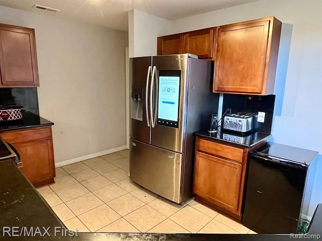 kitchen with stainless steel fridge, dark countertops, light tile patterned floors, and brown cabinetry