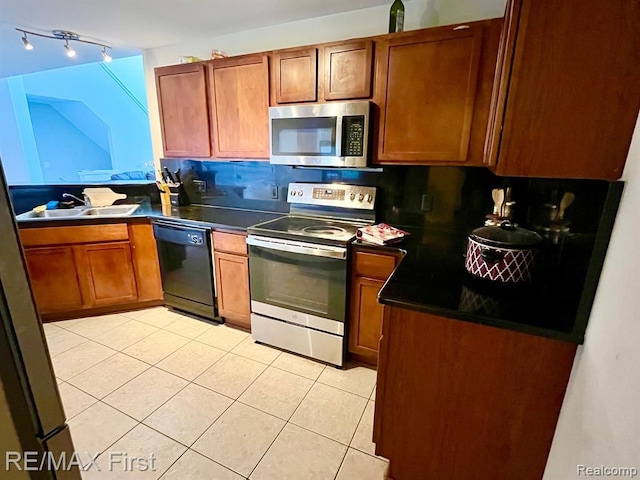 kitchen featuring appliances with stainless steel finishes, dark countertops, light tile patterned flooring, a sink, and brown cabinets