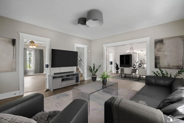 living area with baseboards, stairway, ceiling fan with notable chandelier, and wood finished floors