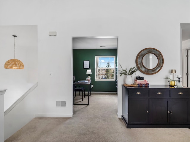 hallway with baseboards, visible vents, and light colored carpet
