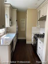 kitchen with a sink, under cabinet range hood, black gas range, light countertops, and baseboards
