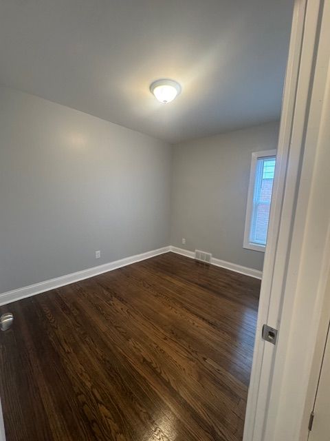 spare room featuring baseboards, dark wood-type flooring, and visible vents