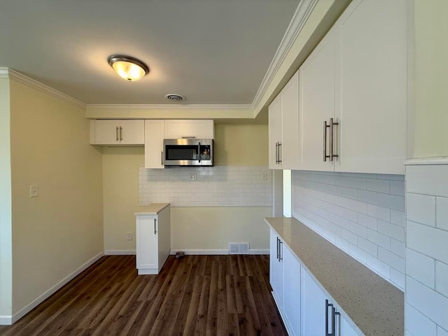 kitchen with dark wood-style flooring, ornamental molding, stainless steel microwave, white cabinetry, and tasteful backsplash