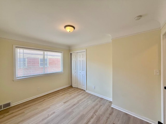 unfurnished bedroom featuring crown molding, a closet, light wood-type flooring, and visible vents