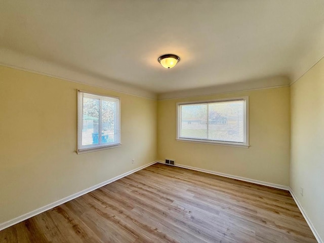 empty room featuring a wealth of natural light, visible vents, wood finished floors, and baseboards
