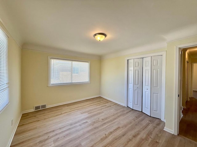 unfurnished bedroom with a closet, light wood-style floors, visible vents, and baseboards