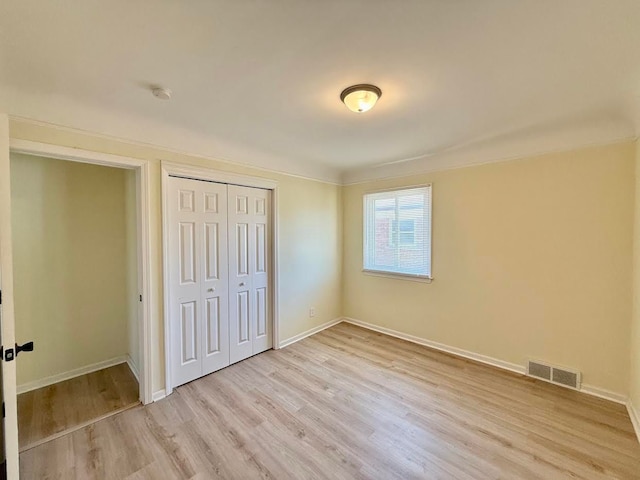 unfurnished bedroom with a closet, baseboards, visible vents, and light wood-style floors