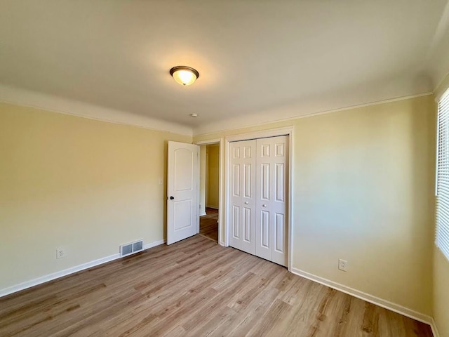 unfurnished bedroom with a closet, crown molding, visible vents, baseboards, and light wood-style floors