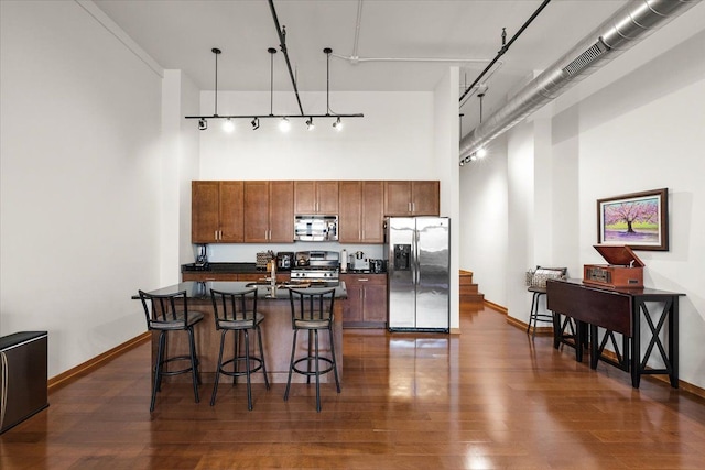 444 W Willis St Unit 204, Detroit, MI 48201 - kitchen with stainless steel appliances, dark countertops, a high ceiling, a breakfast bar area, and dark wood-type flooring