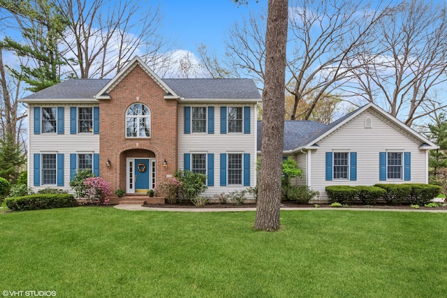 colonial home featuring roof with shingles and a front lawn