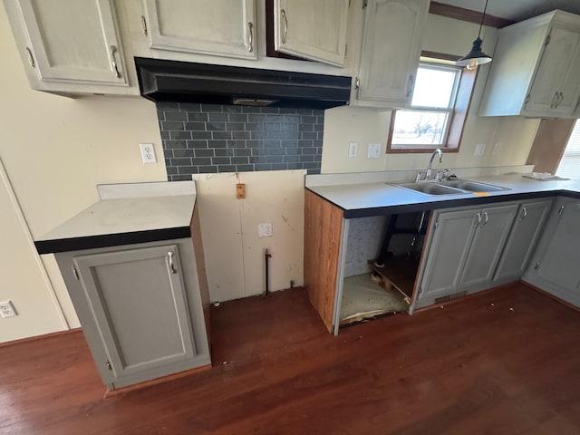 kitchen with under cabinet range hood, dark wood-style flooring, a sink, decorative backsplash, and light countertops