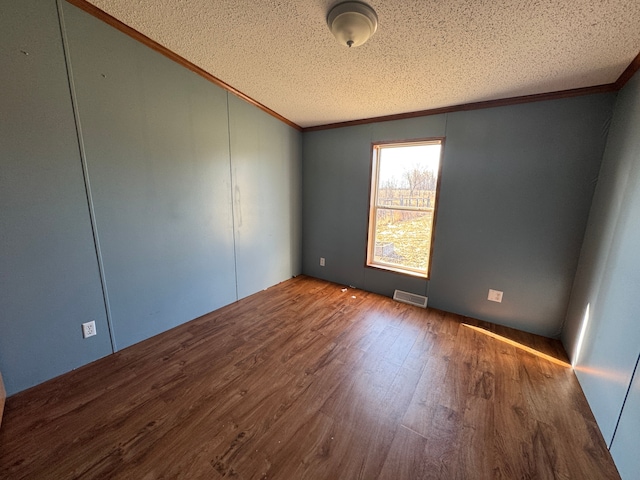empty room featuring a textured ceiling, visible vents, wood finished floors, and ornamental molding
