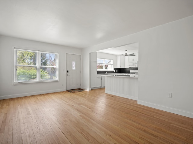 unfurnished living room featuring baseboards, light wood-style floors, a sink, and a ceiling fan